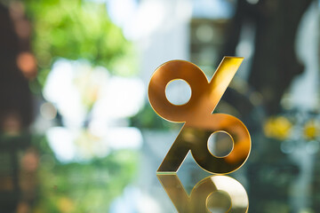 Golden percentage symbol standing on reflective glass surface with blurred green background, representing interest rate, financial growth, investment return, profit margin, and economic value.