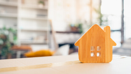 Wooden house icon on cardboard box in cozy home interior, symbolizing moving house, new homeownership, real estate investment, family living, housing market, and property relocation.