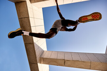 Athletic person jumping dynamically against a unique architectural urban setting under clear skies