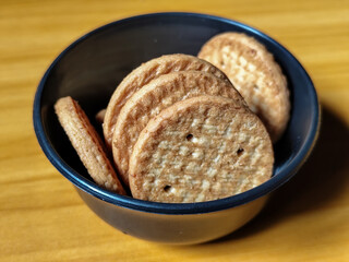 Stack of round wheat crackers in a small black bowl, placed on a wooden table.