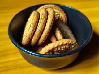 Stack of round wheat crackers in a small black bowl, placed on a wooden table.