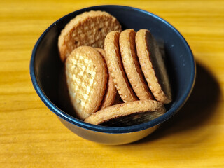 Stack of round wheat crackers in a small black bowl, placed on a wooden table.