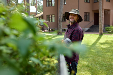 Man pruning garden near a rustic house on a sunny day