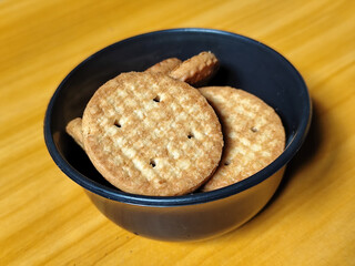 Stack of round wheat crackers in a small black bowl, placed on a wooden table.