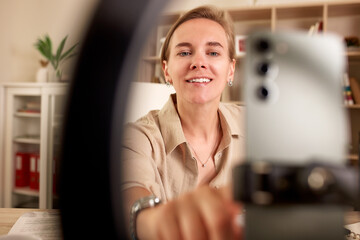 Smiling woman recording video with smartphone in modern bright interior