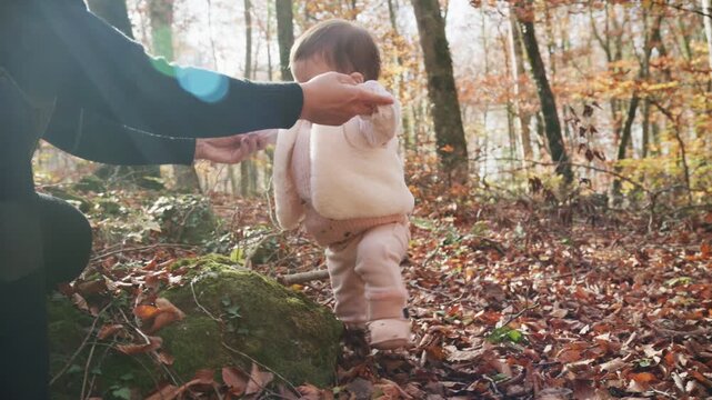Mother helping her baby girl learning to walk in autumn forest