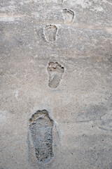 A trail of barefoot prints left in dried cement or concrete, symbolizing childhood, memory, or summer play.