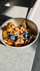 Cereal flakes with blueberries and mango slices served in a white bowl with natural morning light