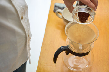 ドリッパーに中細挽きの豆の粉を入れる男性。ペーパードリップでコーヒーを淹れる工程の連続写真。