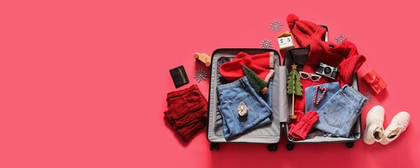 Open suitcase with winter clothes, Christmas decor and accessories on red background with space for...