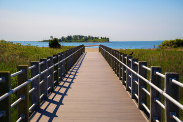 Wooden boardwalk crossing marshland and leading to the beach at Silver Sands State Park in Milford, Connecticut, with Charles Island visible in the background.