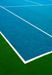 Bright colored tennis court at midday with textured surface and crisp white lines