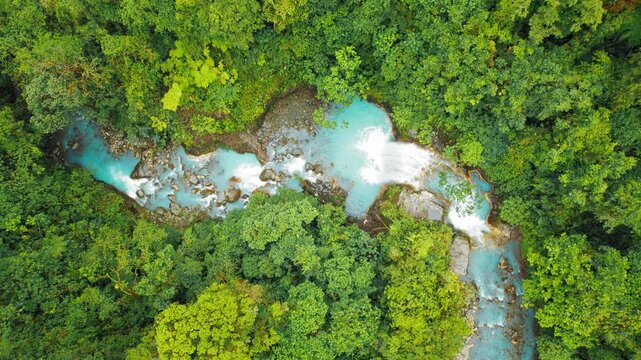 Aerial view of vivid blue waterfall surrounded by lush rainforest in Costa Rica jungle