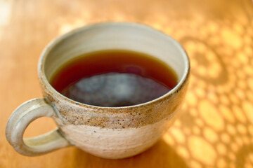 マグカップに入ったコーヒーのクローズアップとレースのカーテンのシルエット。カップの手前にピント