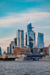 Obraz premium Manhattan skyline, modern buildings, clear sky. Tall glass buildings of Manhattan reflect sunlight over Hudson River in New York City, creating a stunning cityscape.