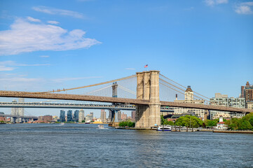 Fototapeta premium Brooklyn Bridge spans East River under clear skies. The Brooklyn Bridge connects Manhattan and Brooklyn, showcasing its iconic architecture against a bright blue sky.