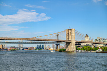 Fototapeta premium Brooklyn Bridge spans the East River in Manhattan. Brooklyn Bridge connects Manhattan to Brooklyn over the East River, showcasing a vibrant skyline and a clear blue sky.