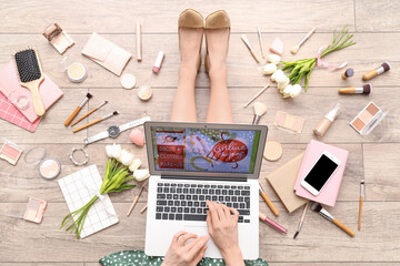 Woman with laptop, makeup products and accessories shopping online on light wooden floor