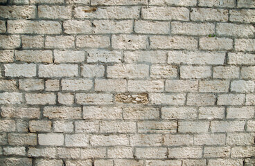Textured wall of rectangular stone blocks in light beige shades and cement between them.