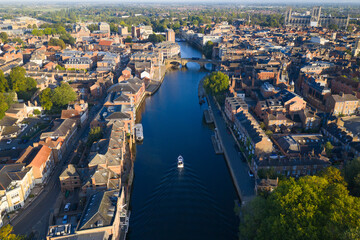 Naklejka premium Aerial image of York showing River Ouse with a boat, bridges, historic rooftops, and York Minster.