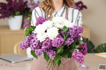 Female florist holding bouquet with lilacs and chrysanthemums in flower shop