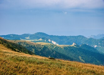 Beautiful panoramic landscape of rolling hills, forested mountains, and rocky ridges under a blue sky. Summer view from alpine meadows in a remote highland region.