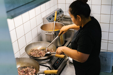 Chef cooking stir-fried vegetables and beef in a wok on a professional kitchen stove. Top-down view of Thai or Asian cuisine in preparation.