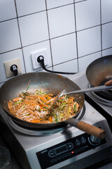 Chef cooking stir-fried vegetables and beef in a wok on a professional kitchen stove. Top-down view of Thai or Asian cuisine in preparation.