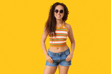 Beautiful African-American woman with sunglasses on yellow background