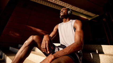 Athletic man relaxing on stairs wearing headphones during a sunny afternoon.