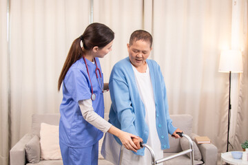 Young nurse assisting senior woman in walking with a walker, demonstrating caregiving,...