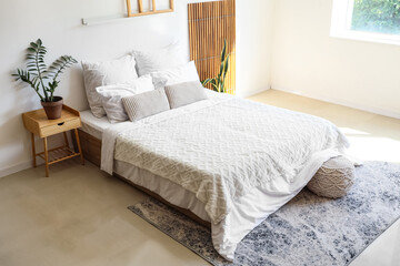 Big comfortable bed, pouf and houseplants in interior of bedroom