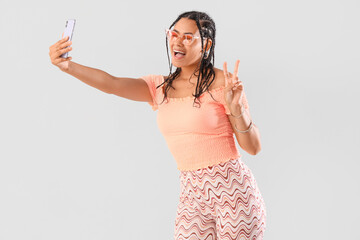 Young African-American woman with dreadlocks taking selfie on light background