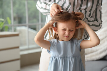 Mother checking her little daughter's head with pediculosis at home