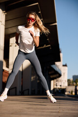 Athletic woman exercising outdoors under bright sunlight wearing sportswear and sunglasses