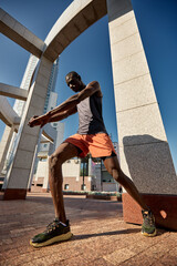 Athlete stretching outdoors under a modern architectural structure on a sunny day