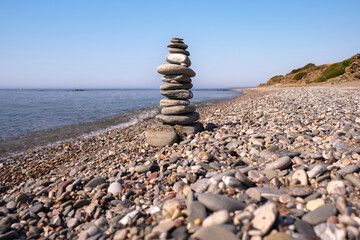 A cairn made out of flat rounded rocks erected on a sunny pebble beach near the water's edge