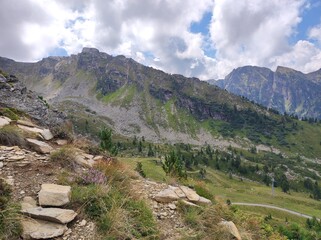 Mountain Path with Rocky Terrain and Lush Hills under Cloudy Sky