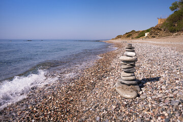 A cairn made out of flat rocks erected with balance at the water's edge next to a seething wave