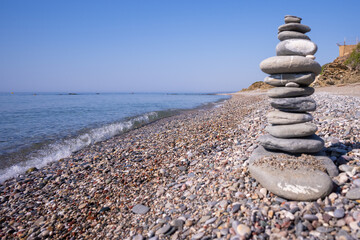 A cairn made out of flat rounded rocks erected on a sunny pebble beach near the water's edge