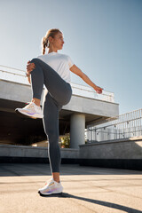 Woman stretching outdoors under bright sunlight in modern urban setting