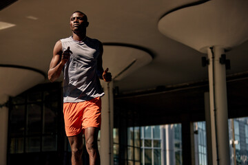Athletic man jogging outdoors under modern urban architecture and daylight