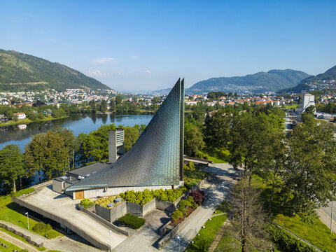 Aerial view of the striking Slettebakken Church with its distinctive triangular roof, nestled beside a serene lake and framed by lush greenery, Slettebakken, Bergen, Norway.