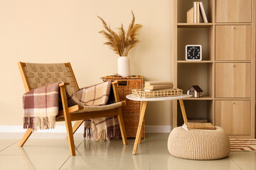 Interior of stylish modern room with armchair, coffee table and shelving unit near beige wall