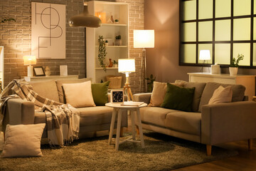 Cozy sofas, coffee table and glowing lamps in interior of living room