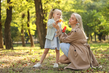 Happy mother with her little daughter blowing soap bubbles in park on autumn day