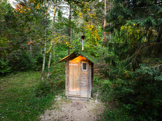 A rustic wooden outhouse or ecological compost toilet stands in a peaceful forest clearing for sustainable, off-grid living.