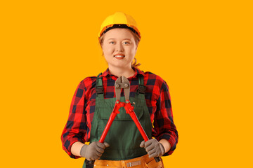 Young female construction worker with bolt cutters on yellow background. Woman in male profession...