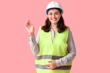 Young female construction worker on pink background. Woman in male profession concept