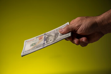 A hand holds dollars on a yellow surface, close - up, money concept